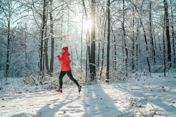 Trail runner woman dressed bright red windproof jacket jogging picturesque snowy forest path during...