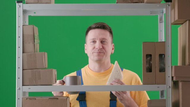 Framed on a green background of chromakey. Depicted an adult man in a work uniform. Demonstrates a storekeeper in a warehouse. He holds a cup of sandwich and eats and smiles, he happy, satisfied