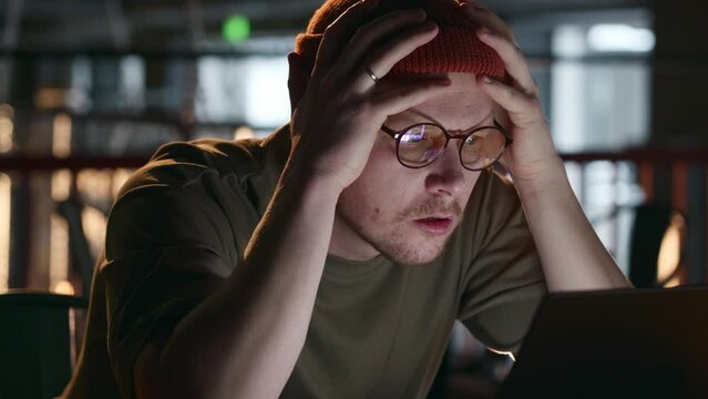 A programmer or hacker hipster millennial looks at the screen in frustration and surprise, holds his head and swears. The developer's reaction to errors in the program code. High quality 4k footage