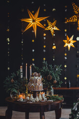 Fototapeta premium Christmas and New Year beautiful elegant family dinner table setting decorated with candles, fir tree branches, handmade craft toys. Gorgeous big homemade cake with gingerbread houses as centrepiece.