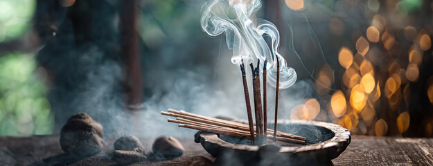Incense sticks emit a serene smoke. Smoke from agarbatti sticks curls into a bokeh-lit background, evoking a sense of calm