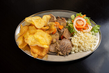 Traditional Portuguese stewed pig's tongue with fries, salad, and rice in a restaurant setting.