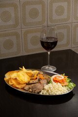 Traditional Portuguese stewed pig's tongue with fries, salad, and rice in a restaurant setting.
