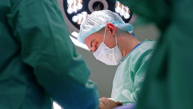 Concentrated look of a surgeon in mask looking at patient. Side view portrait of a doctor working at operation. Low angle view.