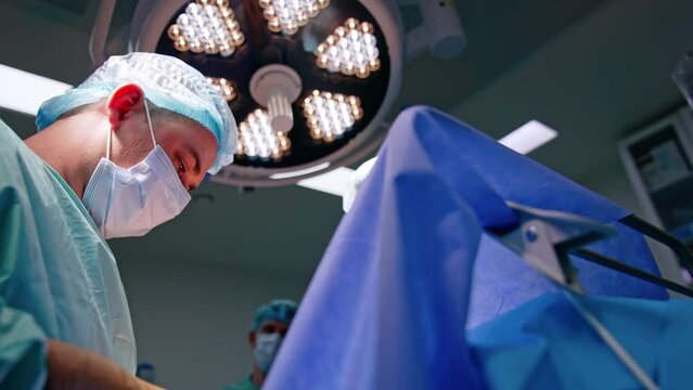 Mid aged male doctor in mask and cap. Low angle view portrait of a surgeon busy with work.