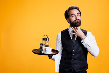 Stylish waiter posing with food tray against yellow background, preparing to serve coffee cup or...