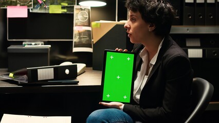 Law agent holds tablet with greenscreen to review classified records and solve mistery. Inspectors team conducting criminal investigation with mockup and isolated chromakey display.
