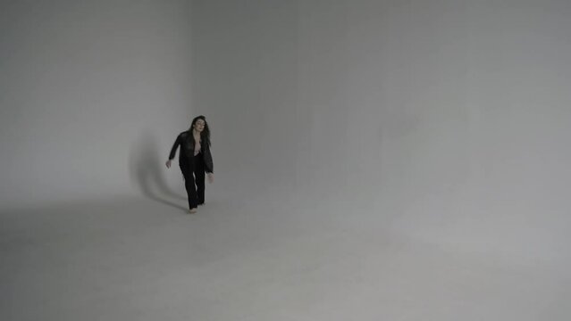 Beautiful curly woman in black clothes dances barefoot on the corner of a cyclorama in a white photo studio