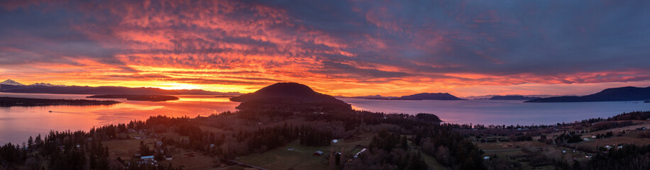 Obraz premium Panoramic Drone View of the South End of Lummi Island During a Spectacular Sunrise. Aerial shot of the sun rising over Bellingham Bay in the northwest corner of Washington state in the Salish Sea.