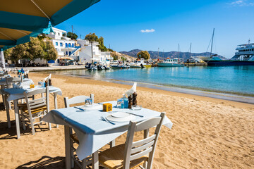 Greek tavern restaurant with tables on beach in Kimolos port, Kimolos island, Cyclades, Greece - 693230196