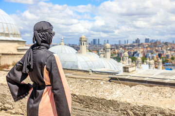 From Suleymaniye Mosque, Islamic woman in traditional Arab hijab dress takes in breathtaking panorama of Istanbul's skyline. Grand mosque, commissioned by Suleiman the Magnificent in 1500s in Turkey.