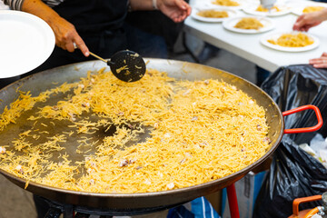 Cook serving into plates traditional Catalan pasta fideua with shrimps and mussels prepared in large paellera at street holiday in Spain, cropped shot..