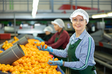 Portrait of smiling woman worker of fruit processing factory checking fresh ripe tangerines on...