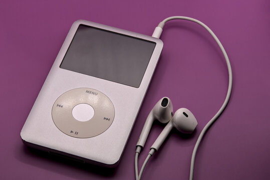 Apple Ipod classic mp3 player with white headphones on a solid pink background.