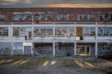 Facade of a derelict former factory building with broken windows, missing roof, streaks of sun in...
