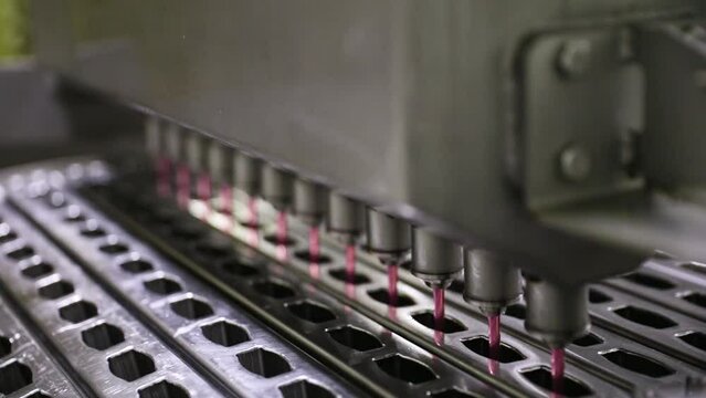 Industrial ice cream production process and manufacturing. Technology and automation. Closeup view of a commercial popsicle production machine filling the ice pop molds with strawberry flavor.