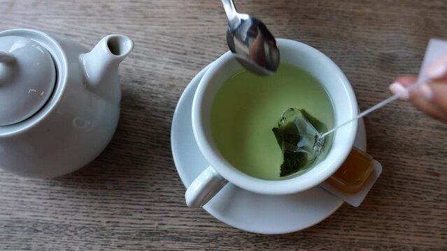 Girl manicure hand hold green tea bag in ceramic cup and stir in water