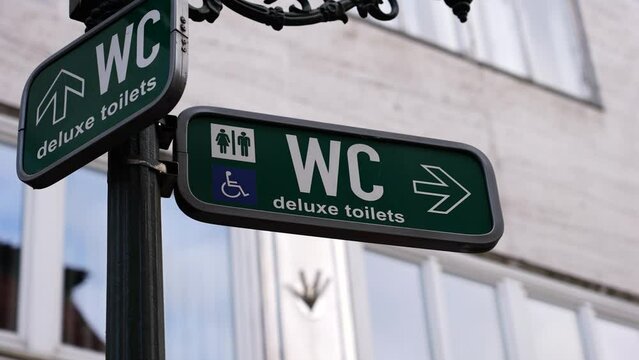 Green sign on street pole show direction to public toilet location, Prague