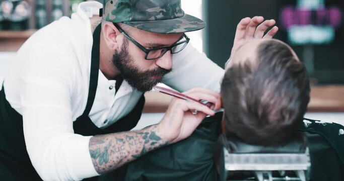 Salon, shave or grooming with a barber and man in a seat as a customer for luxury or professional service. Industry, skill or hairdresser and person shaving the beard of a client with a minora blade