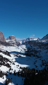 Gardena Pass and Mountains on Sunny Winter Day. South Tyrol, Dolomites, Italy. Aerial View . Drone Flies Backwards. Vertical Video