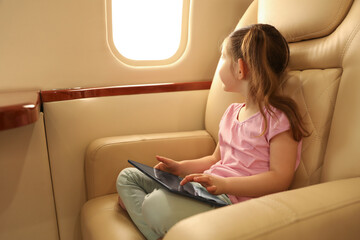 Cute little girl using tablet in airplane during flight - obrazy, fototapety, plakaty