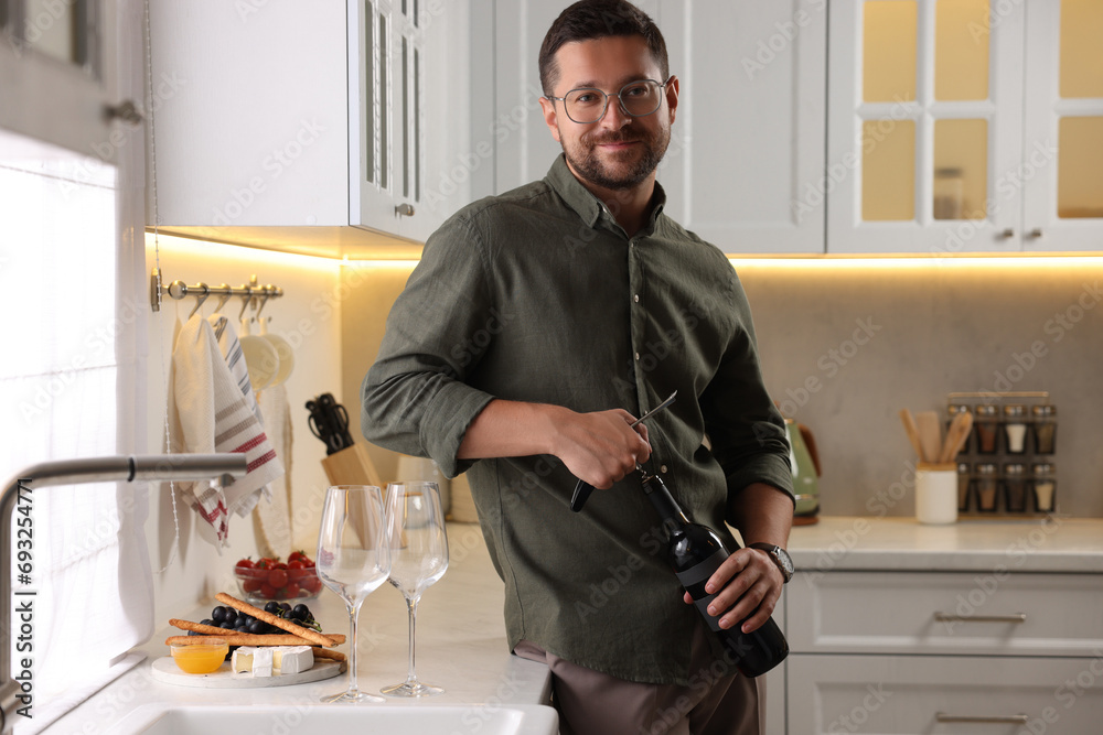 Poster Romantic dinner. Man opening wine bottle with corkscrew in kitchen