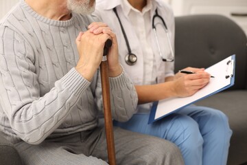 Nurse with clipboard assisting elderly patient on sofa indoors, closeup