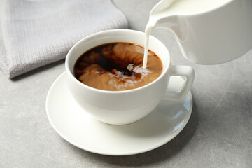 Pouring milk into cup of hot coffee on grey table