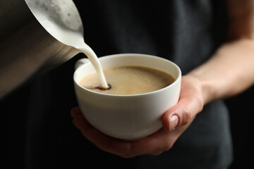 Woman pouring milk into cup of hot coffee, closeup