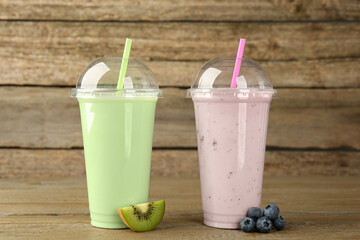 Plastic cups with different tasty smoothies and fresh fruits on wooden table
