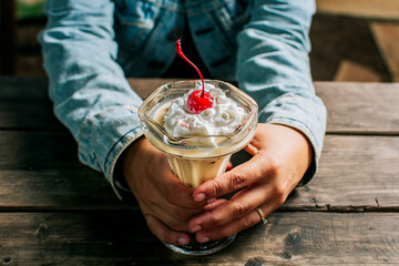 Female hand holding cherry milkshake on wooden table. Person holding cherry smoothie over wooden...