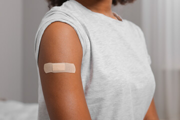 Young woman with adhesive bandage on her arm after vaccination indoors, closeup