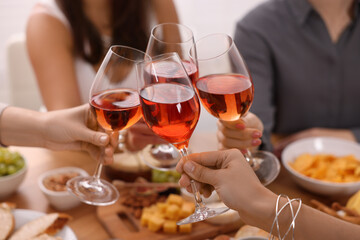 People clinking glasses with rose wine above wooden table indoors, closeup - Powered by Adobe
