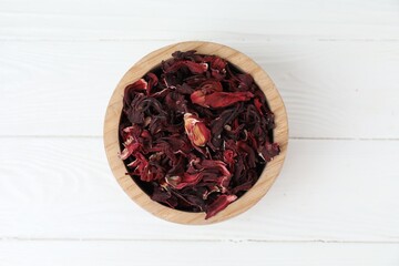Hibiscus tea. Bowl with dried roselle calyces on white wooden table, top view