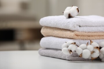 Fototapeta na wymiar Terry towels and cotton branch with fluffy flowers on white table indoors, closeup. Space for text