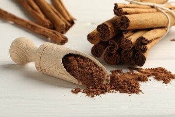 Dry aromatic cinnamon sticks, powder and scoop on white wooden table, closeup