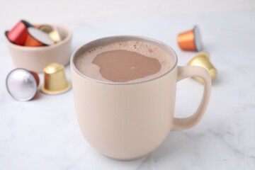 Cup of coffee and capsules on white marble table, closeup
