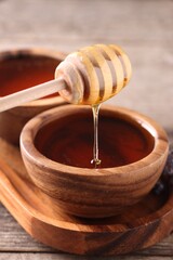 Pouring delicious honey from dipper into bowl on wooden table, closeup