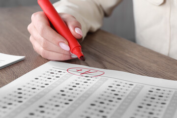 School grade. Teacher writing letter A with plus symbol on answer sheet at wooden table, closeup