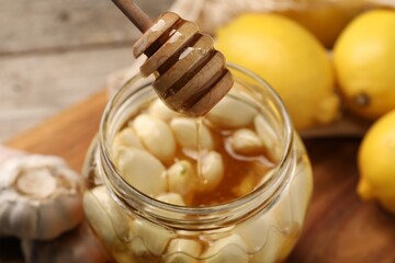 Natural honey dripping from dipper into glass jar with garlic on table, closeup