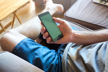 Young man using mobile phone while sitting at home on the sofa i