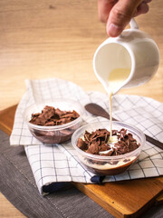 A hand pouring milk into chocolate pudding with coco-crunch topping