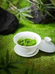 Green tea and cup on the grass, creative outdoor photography, green background, Chinese tea leaves