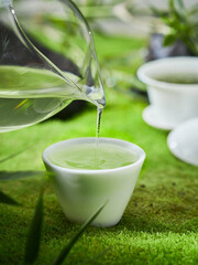 Green tea and cup on the grass, creative outdoor photography, green background, Chinese tea leaves