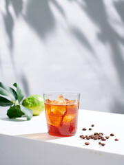 Cold brew coffee shot indoors, textured glass refracts light, sun dappled shadow background