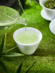 Green tea and cup on the grass, creative outdoor photography, green background, Chinese tea leaves