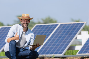 young male technician in sun hat and shirt holding laptop and checking solar panels while standing...