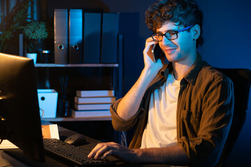 Young businessman calling on smartphone to customer or coworker, looking at computer screen of...