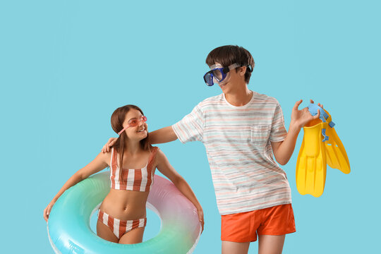 Cute children with inflatable ring and flippers on blue background
