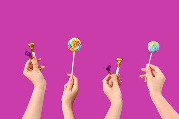 Female hands with party blowers and candies on purple background